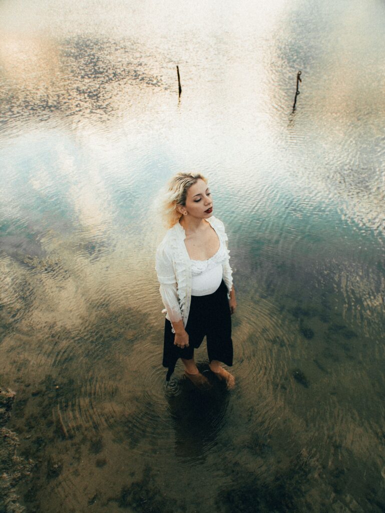 Woman using the anxiety relief exercise of guided imagery by imagining she is standing in the shallow waters of a peaceful lake.
