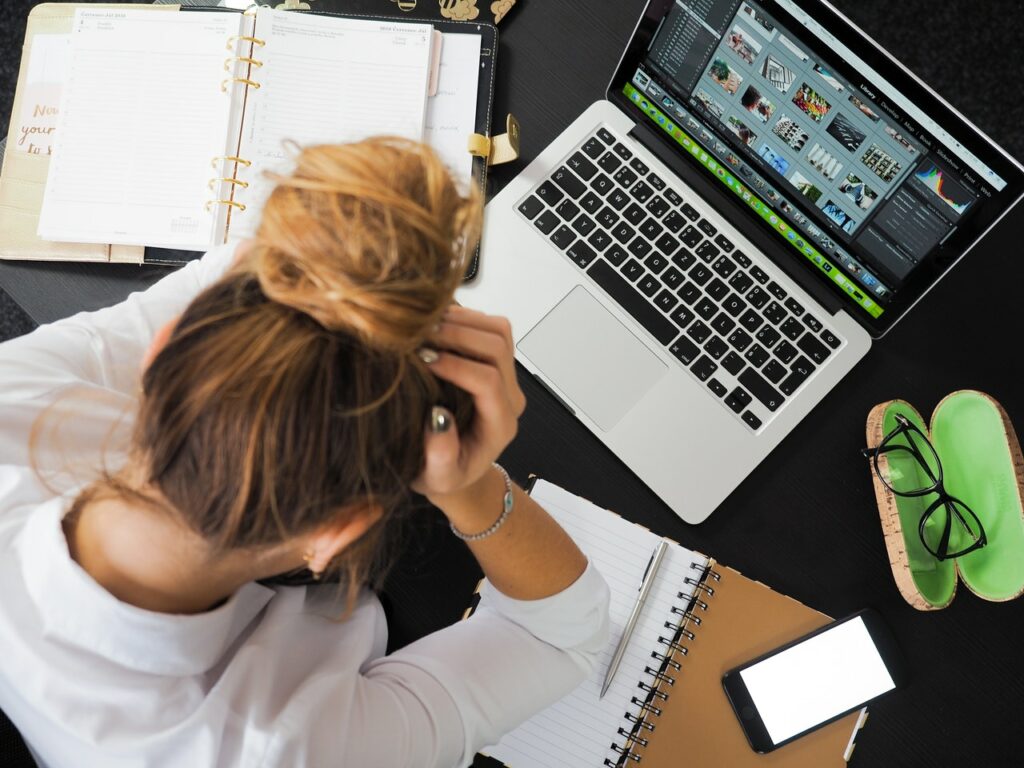 Overwhelmed white business woman with her head in her hands in need of good coping skills to calm workplace pressure.