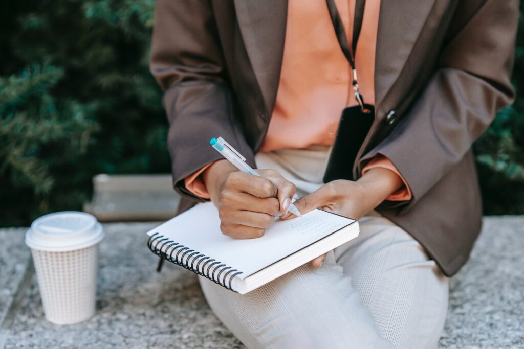 Woman sitting outside her place of work practicing an emotional coping skill of journaling in a notebook.