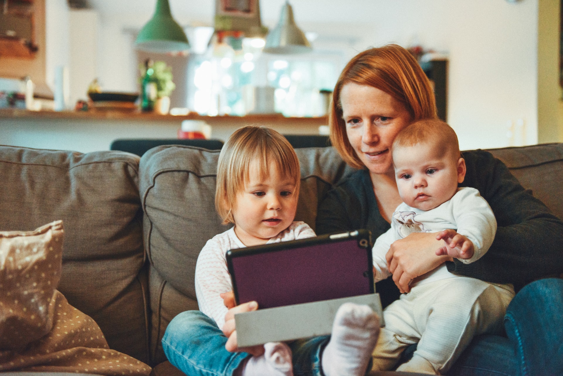 Mom sitting next to toddler and holding baby looking at parenting advice for new parents on computer