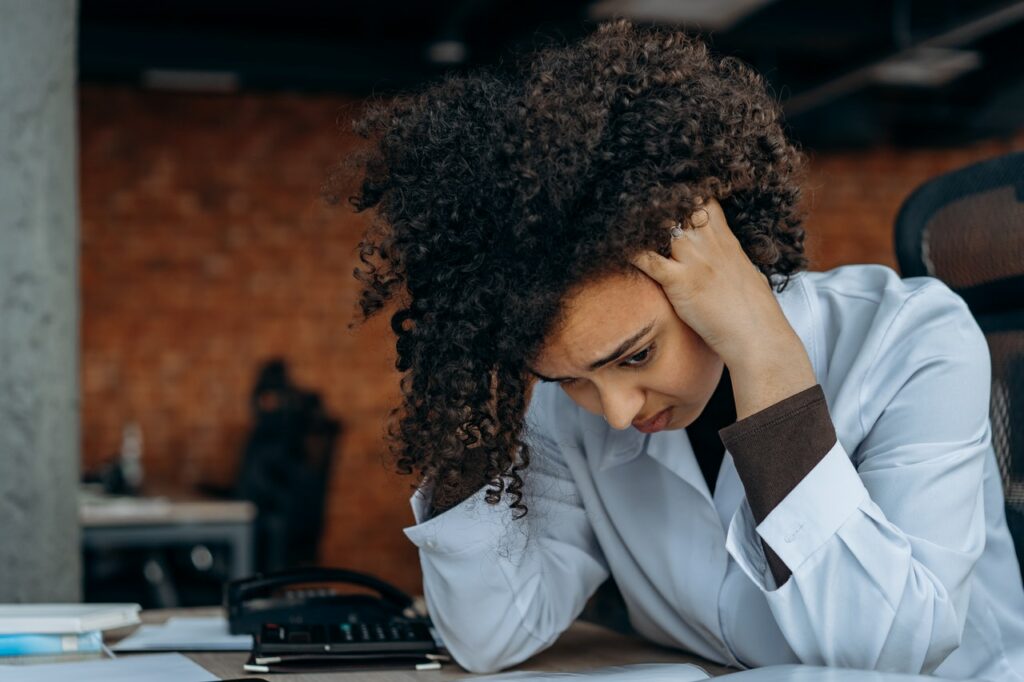 Black woman sitting with her head in her hands feeling overwhelmed at work.