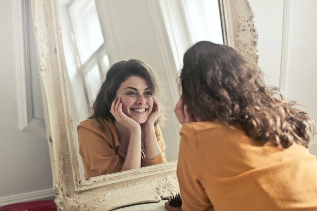 Woman smiling in a mirror not letting harmful self-criticism get in the way of her success.