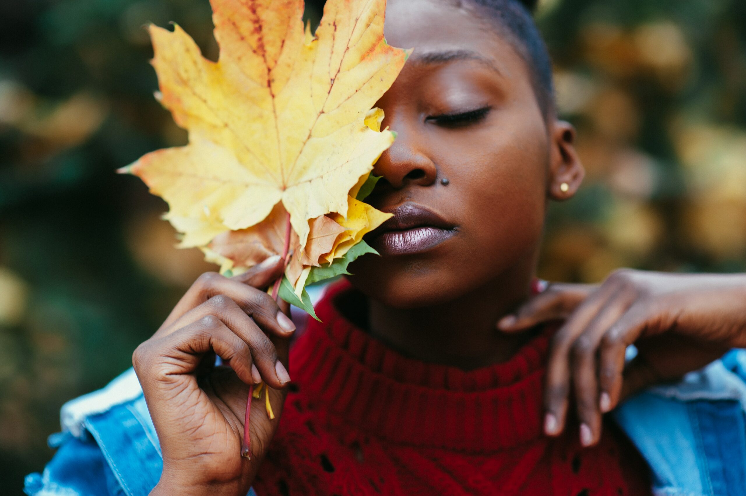 Black woman with eyes closed holding colored leaves